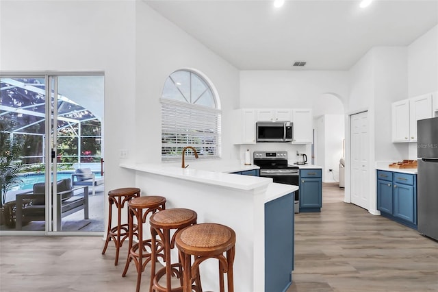 kitchen featuring a kitchen bar, appliances with stainless steel finishes, kitchen peninsula, blue cabinetry, and white cabinetry