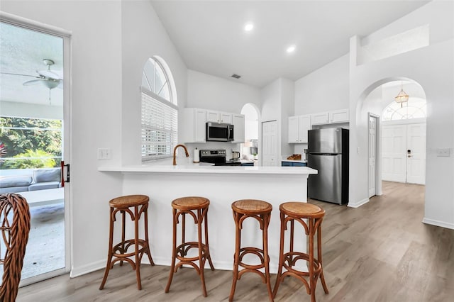 kitchen with white cabinets, ceiling fan, light wood-type flooring, appliances with stainless steel finishes, and kitchen peninsula