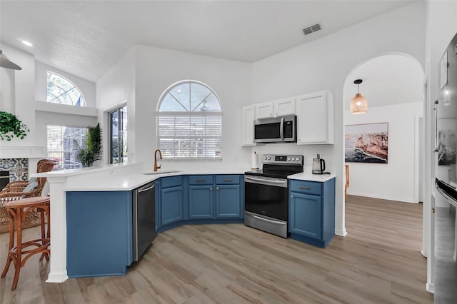 kitchen featuring blue cabinetry, sink, hanging light fixtures, stainless steel appliances, and kitchen peninsula