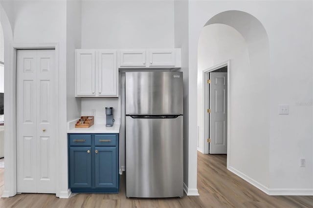 kitchen featuring white cabinets, stainless steel fridge, light wood-type flooring, and blue cabinetry