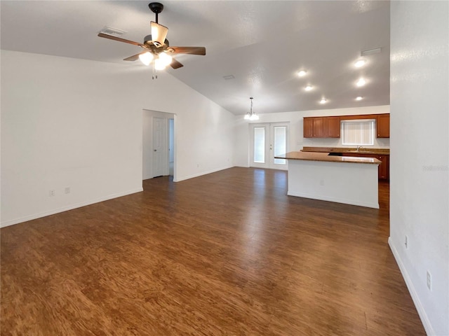 unfurnished living room featuring ceiling fan with notable chandelier, sink, dark wood-type flooring, and vaulted ceiling