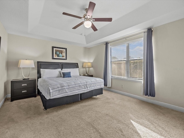 bedroom featuring ceiling fan, light colored carpet, and a tray ceiling