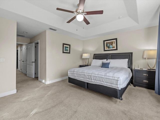 bedroom with light carpet, a tray ceiling, and ceiling fan