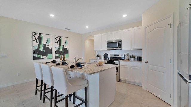 kitchen with white cabinets, sink, light stone countertops, an island with sink, and stainless steel appliances