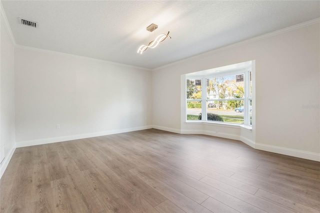 empty room with a textured ceiling, light hardwood / wood-style floors, and ornamental molding