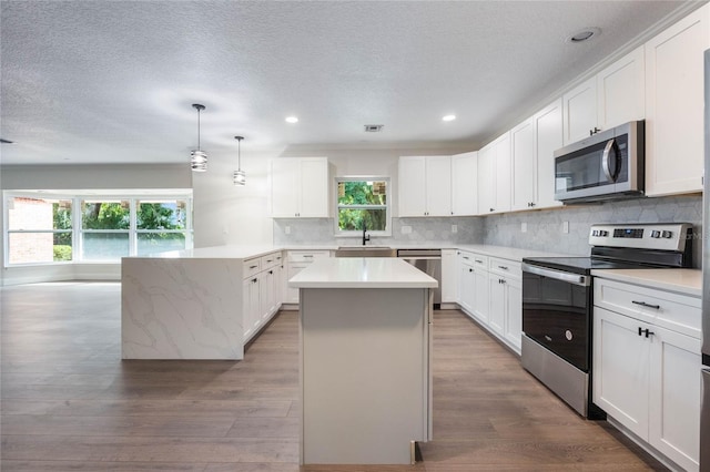 kitchen featuring light wood-type flooring, appliances with stainless steel finishes, a center island, and a healthy amount of sunlight