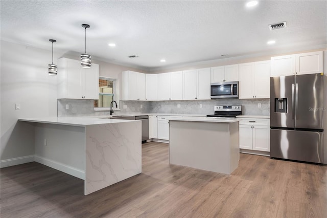 kitchen with white cabinets, kitchen peninsula, decorative light fixtures, wood-type flooring, and stainless steel appliances