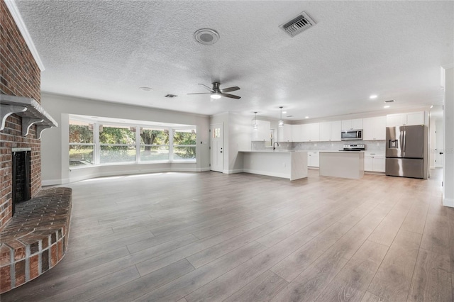 unfurnished living room featuring ceiling fan, sink, a brick fireplace, a textured ceiling, and light wood-type flooring