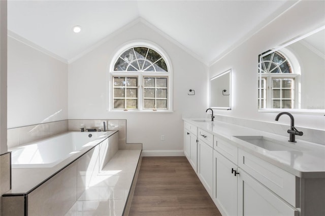 bathroom featuring a bath, crown molding, wood-type flooring, vaulted ceiling, and vanity