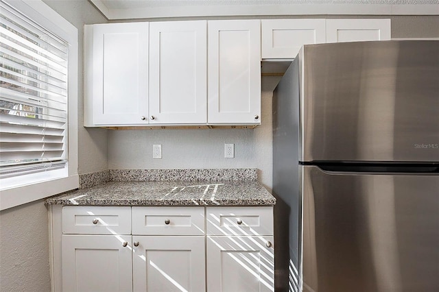 kitchen with stainless steel refrigerator, dark stone countertops, and white cabinets