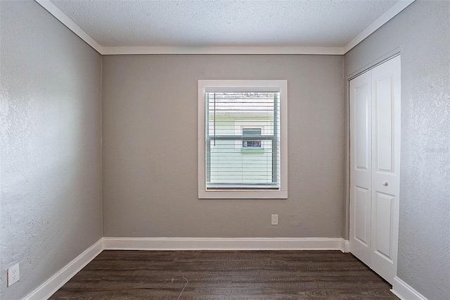 empty room featuring a textured ceiling, ornamental molding, and dark wood-type flooring