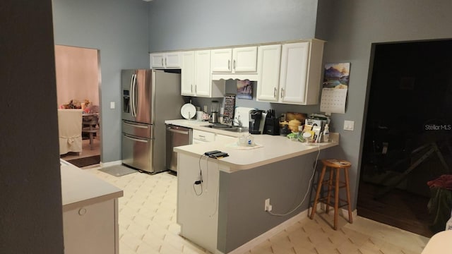 kitchen featuring kitchen peninsula, stainless steel appliances, a breakfast bar, white cabinets, and sink