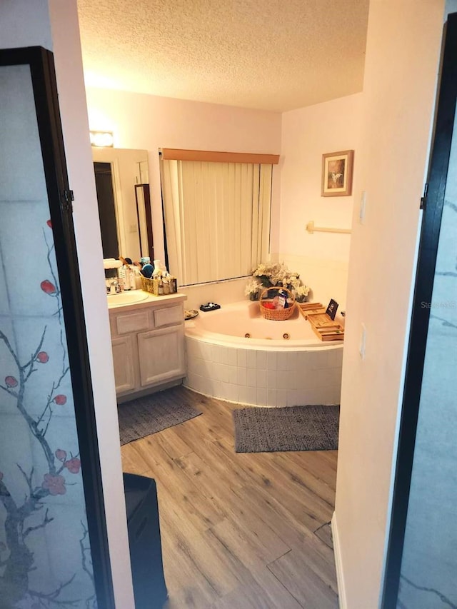 bathroom featuring vanity, a textured ceiling, hardwood / wood-style floors, and a relaxing tiled tub