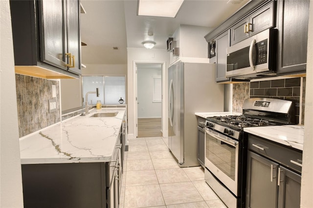 kitchen with sink, decorative backsplash, light tile patterned floors, light stone counters, and stainless steel appliances