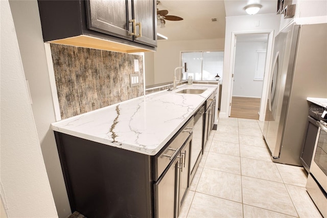 kitchen featuring light stone counters, dark brown cabinetry, ceiling fan, light tile patterned floors, and stainless steel refrigerator