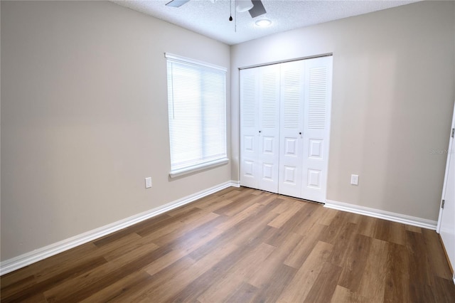 unfurnished bedroom featuring a closet, a textured ceiling, hardwood / wood-style flooring, and ceiling fan