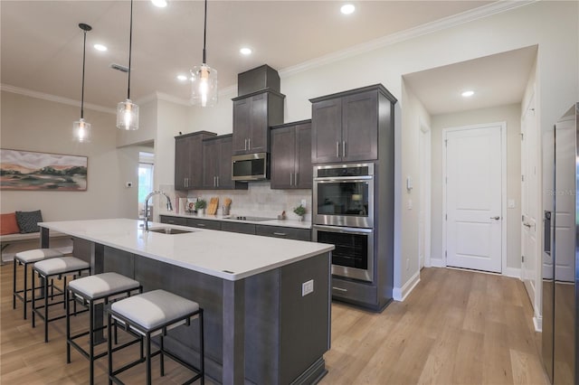 kitchen featuring light wood-type flooring, stainless steel appliances, sink, pendant lighting, and an island with sink