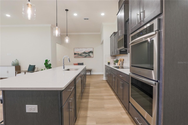 kitchen featuring pendant lighting, a kitchen island with sink, sink, light hardwood / wood-style flooring, and double oven