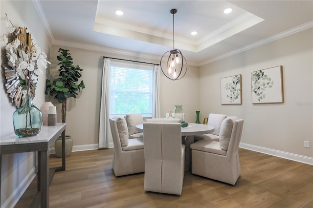 dining space with hardwood / wood-style floors, a raised ceiling, and crown molding