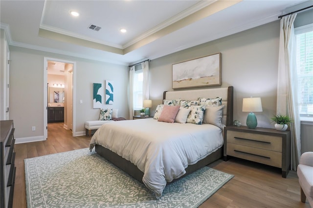 bedroom with a raised ceiling, ensuite bathroom, crown molding, and wood-type flooring