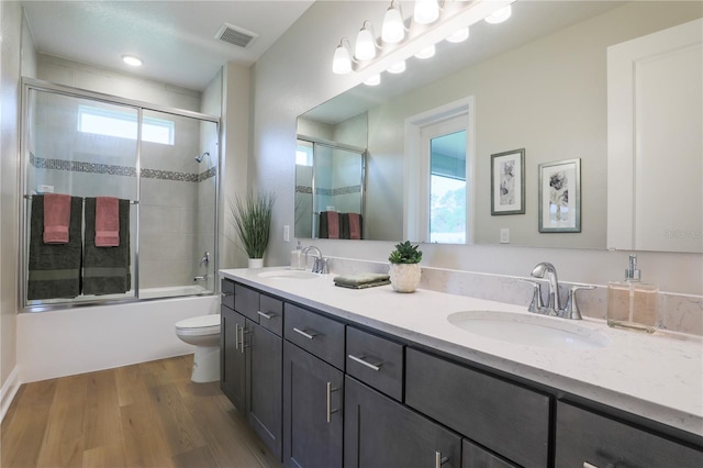 full bathroom with hardwood / wood-style flooring, combined bath / shower with glass door, toilet, and vanity