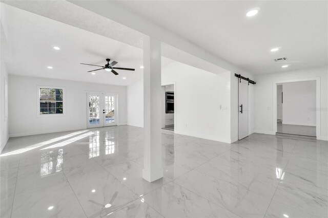 unfurnished living room with a barn door, ceiling fan, and french doors