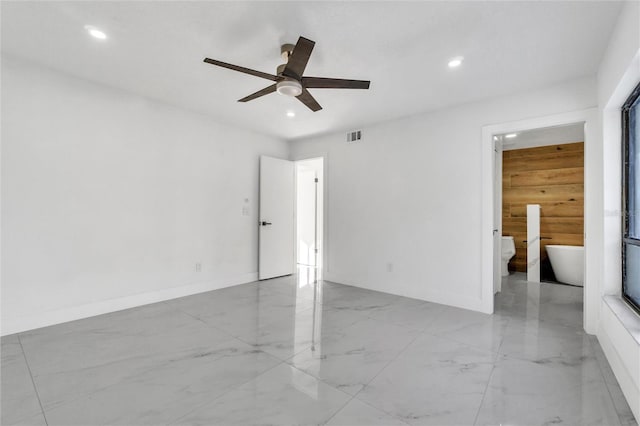 unfurnished bedroom featuring ceiling fan, ensuite bath, and wooden walls