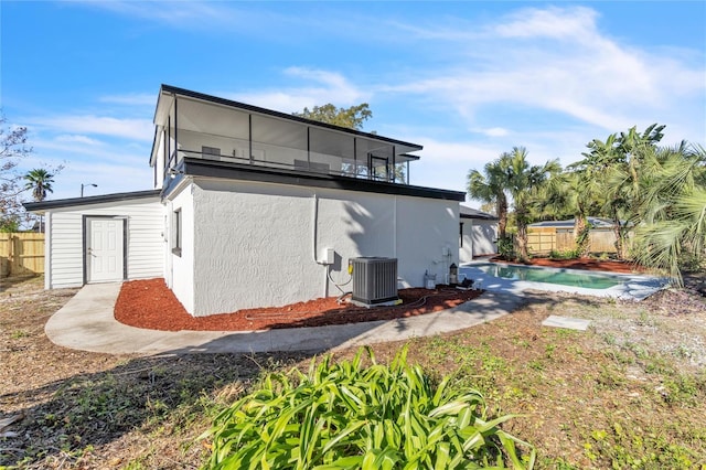 back of house with central AC, a balcony, and a fenced in pool