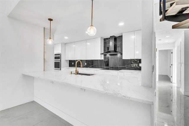 kitchen with wall chimney range hood, hanging light fixtures, sink, and kitchen peninsula