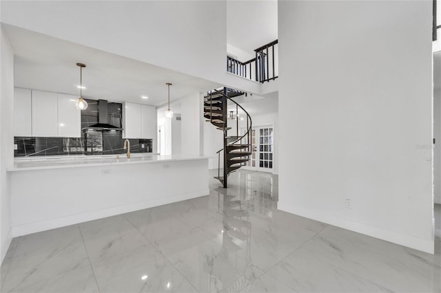 kitchen with white cabinets, backsplash, hanging light fixtures, kitchen peninsula, and wall chimney range hood