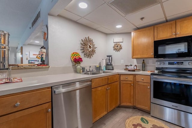 kitchen featuring a paneled ceiling, light wood-type flooring, sink, and appliances with stainless steel finishes