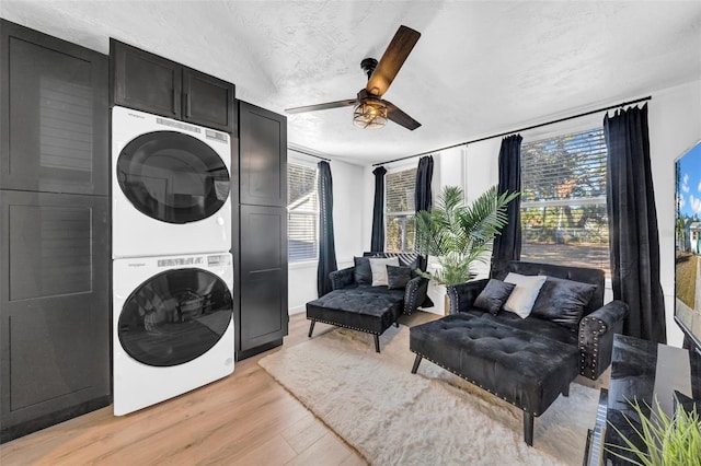 laundry room with ceiling fan, light hardwood / wood-style flooring, stacked washing maching and dryer, and a textured ceiling