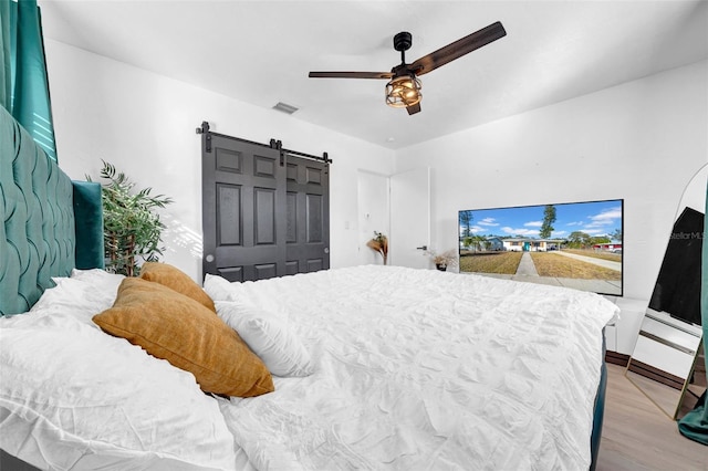 bedroom with a closet, a barn door, light hardwood / wood-style floors, and ceiling fan