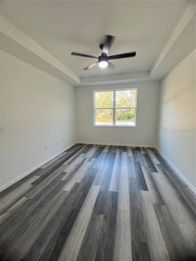 spare room featuring a tray ceiling, ceiling fan, and dark wood-type flooring