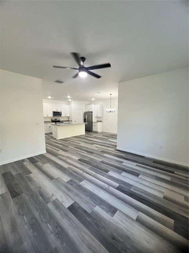 unfurnished living room with dark wood-type flooring and ceiling fan with notable chandelier