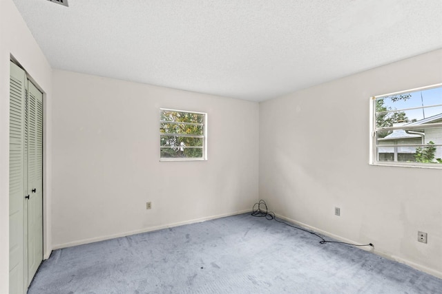 unfurnished bedroom with a textured ceiling, a closet, light colored carpet, and multiple windows