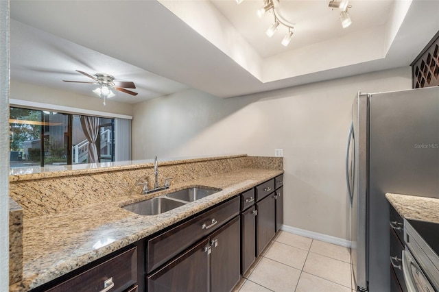 kitchen with appliances with stainless steel finishes, light stone counters, dark brown cabinets, sink, and light tile patterned floors