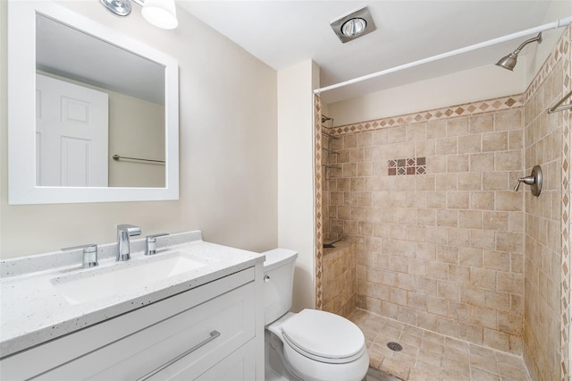 bathroom featuring toilet, a tile shower, and vanity