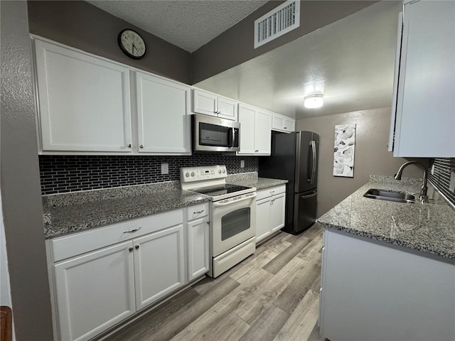 kitchen with white cabinetry, sink, stainless steel appliances, dark stone counters, and light wood-type flooring