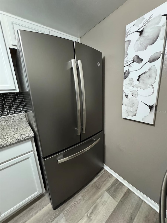 interior details featuring white cabinets, light hardwood / wood-style flooring, light stone countertops, tasteful backsplash, and stainless steel refrigerator