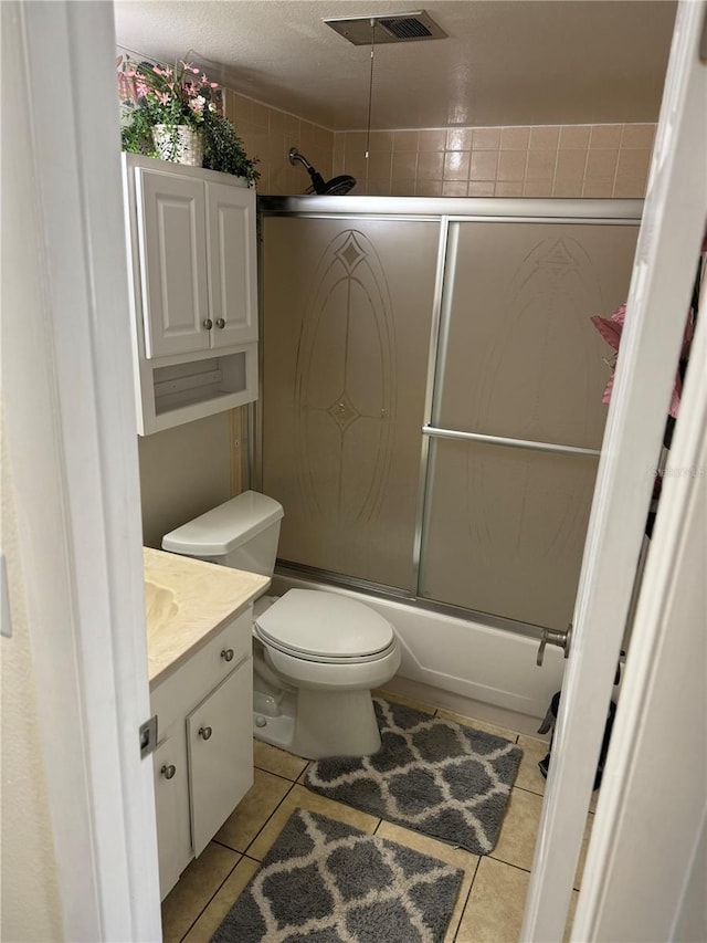 full bathroom with vanity, tile patterned floors, bath / shower combo with glass door, toilet, and a textured ceiling