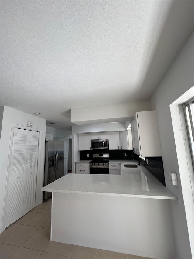 kitchen featuring white cabinetry, kitchen peninsula, stainless steel appliances, and light tile patterned floors