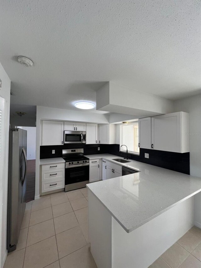 kitchen with kitchen peninsula, appliances with stainless steel finishes, white cabinets, and light tile patterned floors