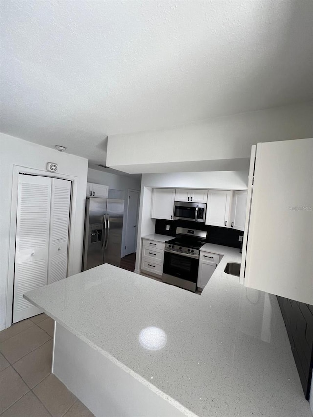 kitchen with kitchen peninsula, appliances with stainless steel finishes, light tile patterned floors, and white cabinetry