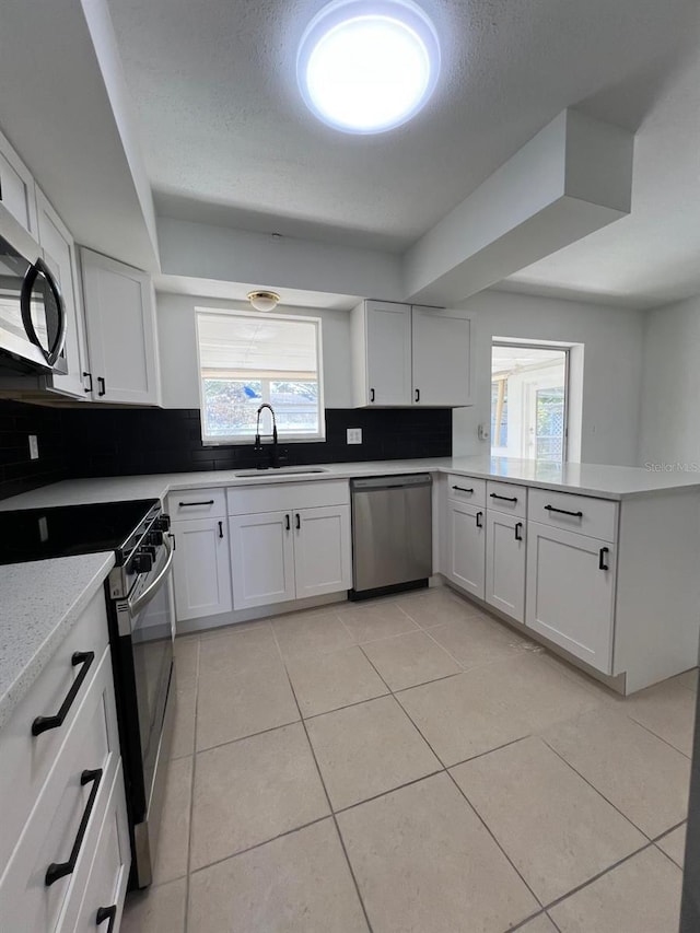 kitchen with sink, decorative backsplash, light tile patterned floors, appliances with stainless steel finishes, and white cabinetry