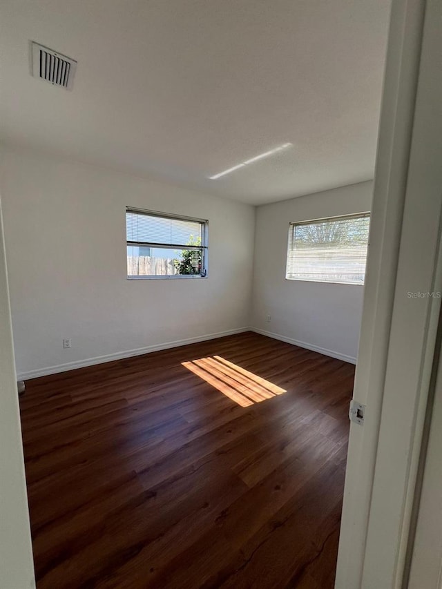 empty room featuring plenty of natural light and dark hardwood / wood-style floors