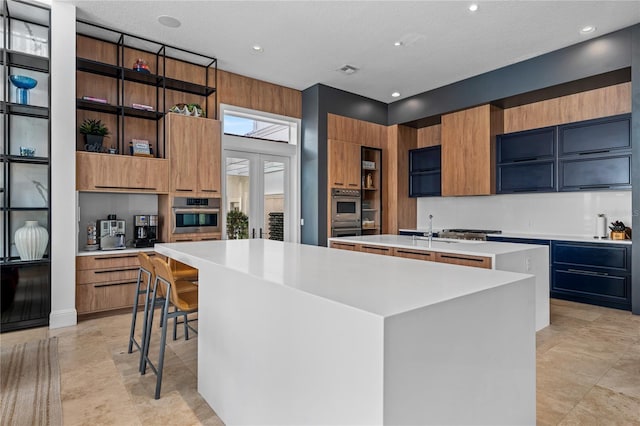 kitchen featuring a spacious island, sink, a textured ceiling, double oven, and a kitchen bar