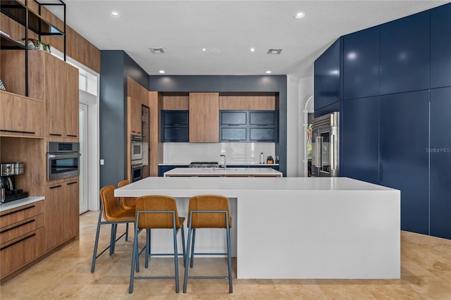 kitchen featuring a kitchen bar, decorative backsplash, a textured ceiling, stainless steel built in fridge, and an island with sink