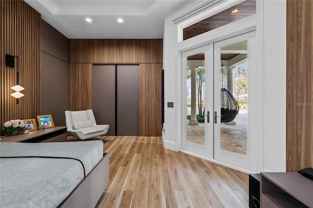 bedroom featuring access to exterior, french doors, light wood-type flooring, elevator, and wood walls