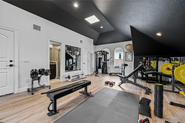 workout area with high vaulted ceiling, a textured ceiling, and light wood-type flooring